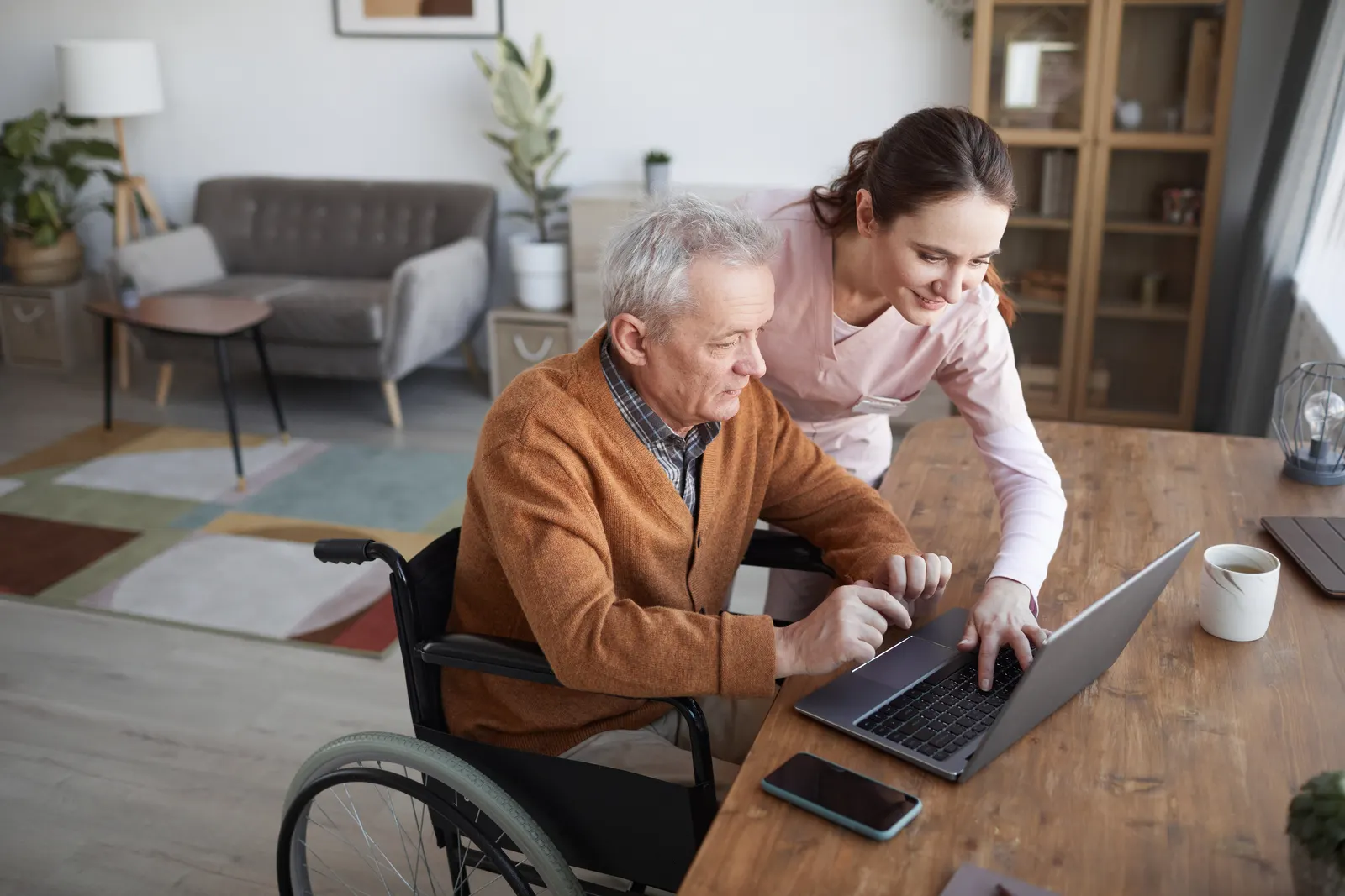 A caregiver helping an older man in a wheelchair at his kitchen table