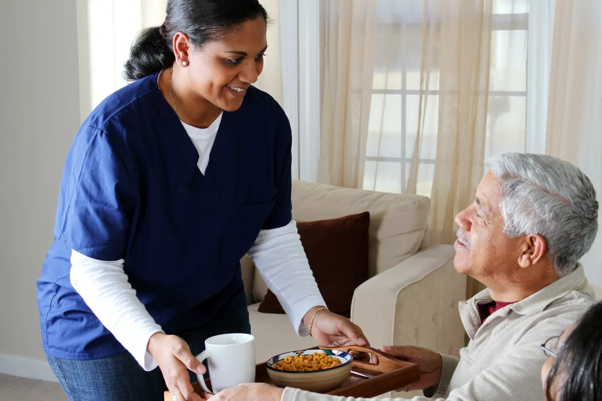 A nurse bringing a meal and medications to an older man at home